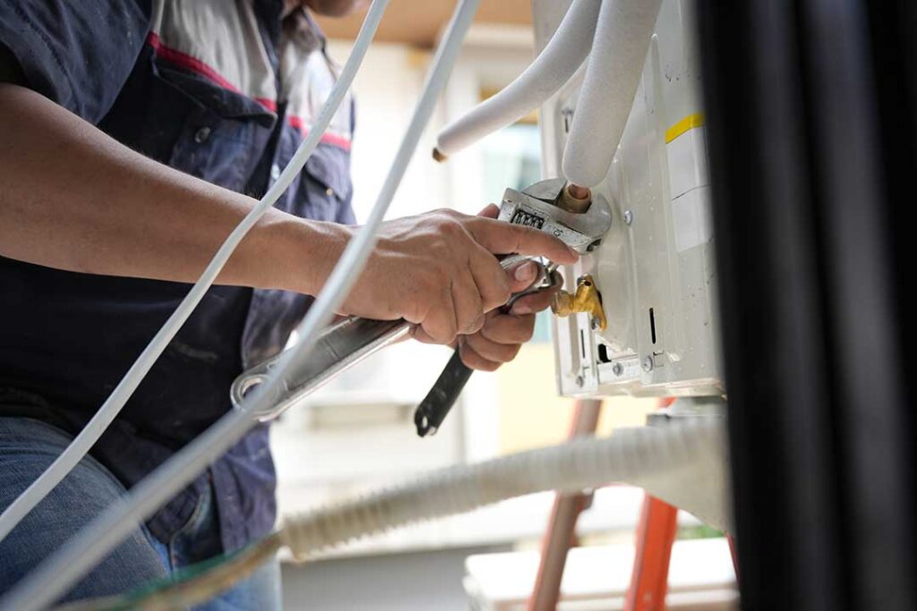 A homeowner inspecting a wall-mounted air conditioning unit for unusual leaks and listening for noise changes.