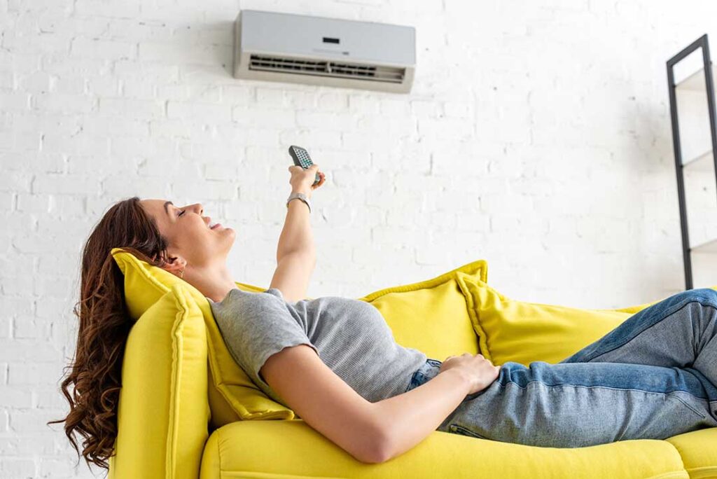 A hand adjusting a digital thermostat on a neutral-colored wall inside a residential home.
