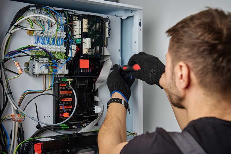 Technician measures a basement furnace beside ductwork, tools, thermostat, and replacement equipment.